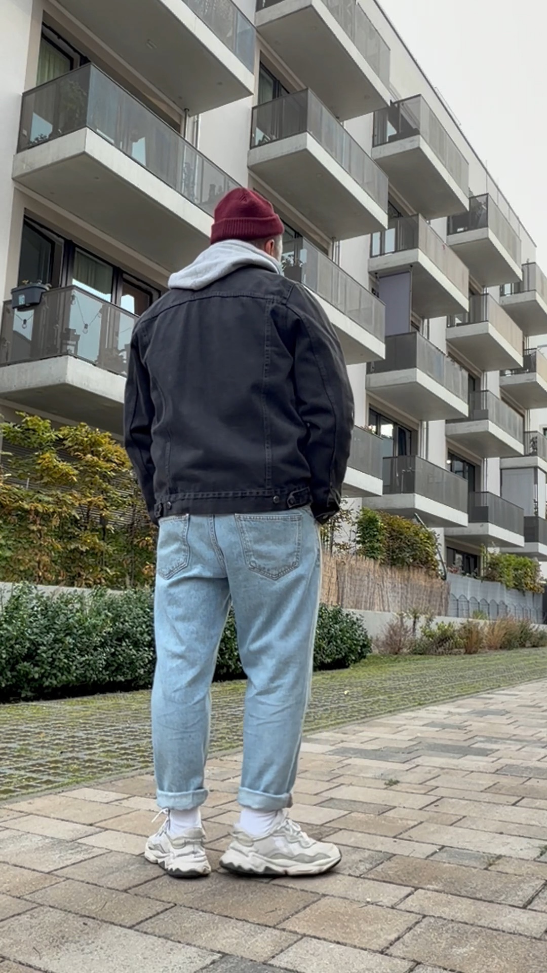 Entspannter Herbst-Look mit grauem Hoodie, schwarzer Denimjacke, hellblauer Jeans im Loose Fit und weißen Sneakern