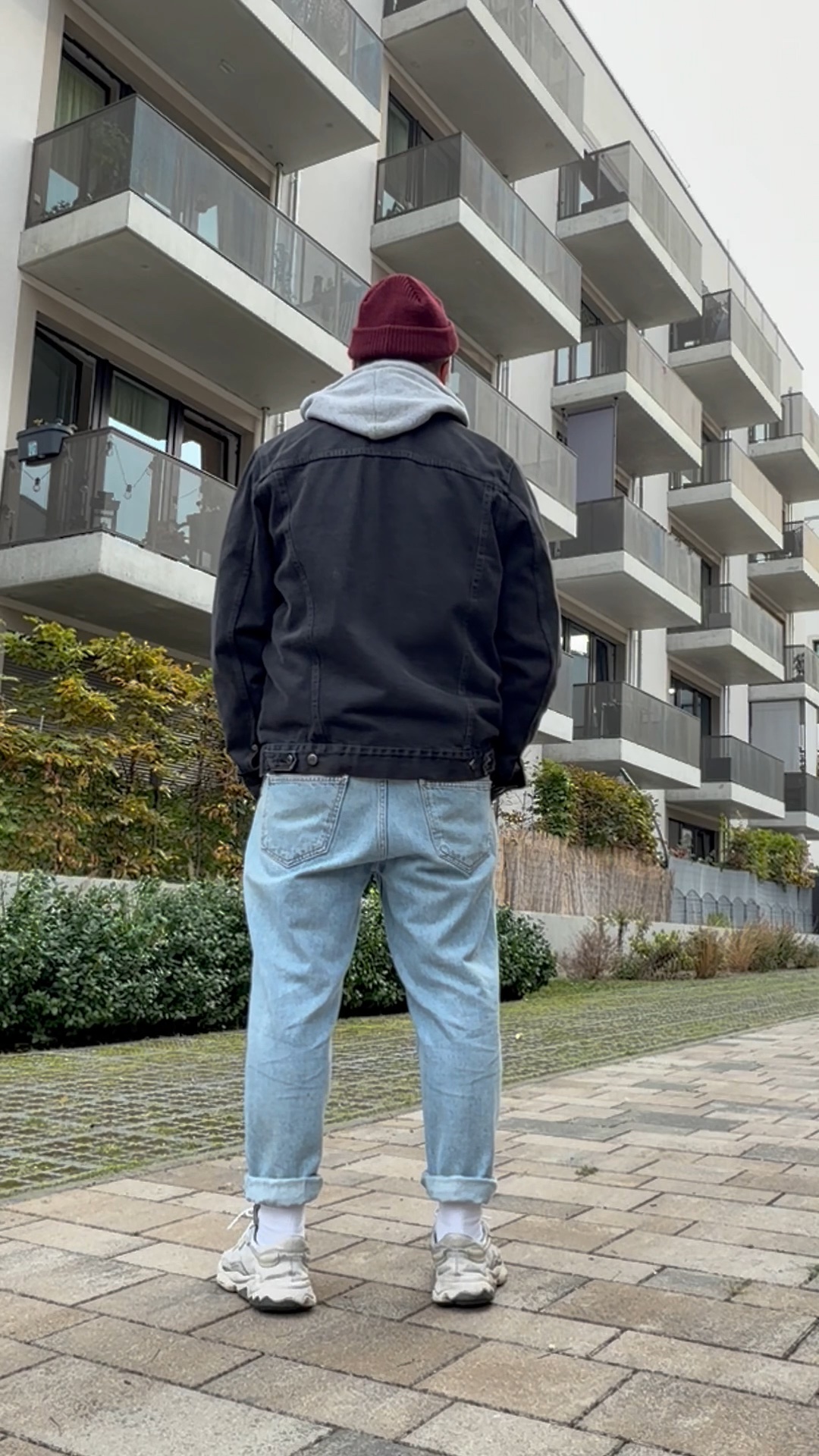 Schwarze Denimjacke über grauem Hoodie kombiniert mit hellblauer Baggy Jeans, weißen Socken und Retro-Sneakern