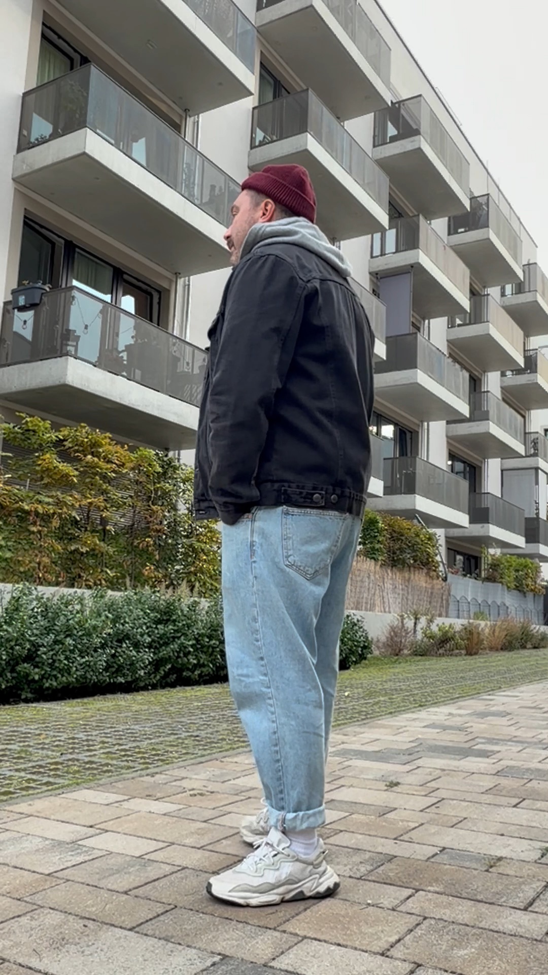 Herbstlicher Streetstyle für Männer mit schwarzer Jeansjacke, grauem Kapuzenpullover und locker geschnittener Jeans mit umgeschlagenen Hosenbeinen