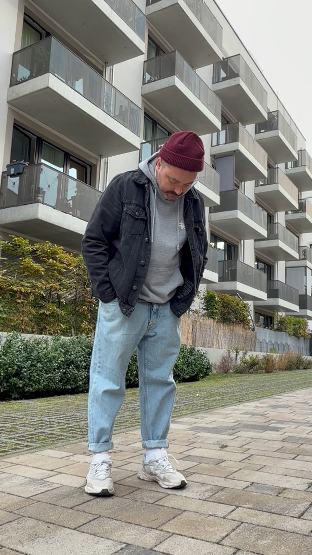 Moderner Herren-Streetwear-Look im Herbst mit schwarzer Denimjacke über grauem Hoodie, weiter Jeans und weißen Sneakern