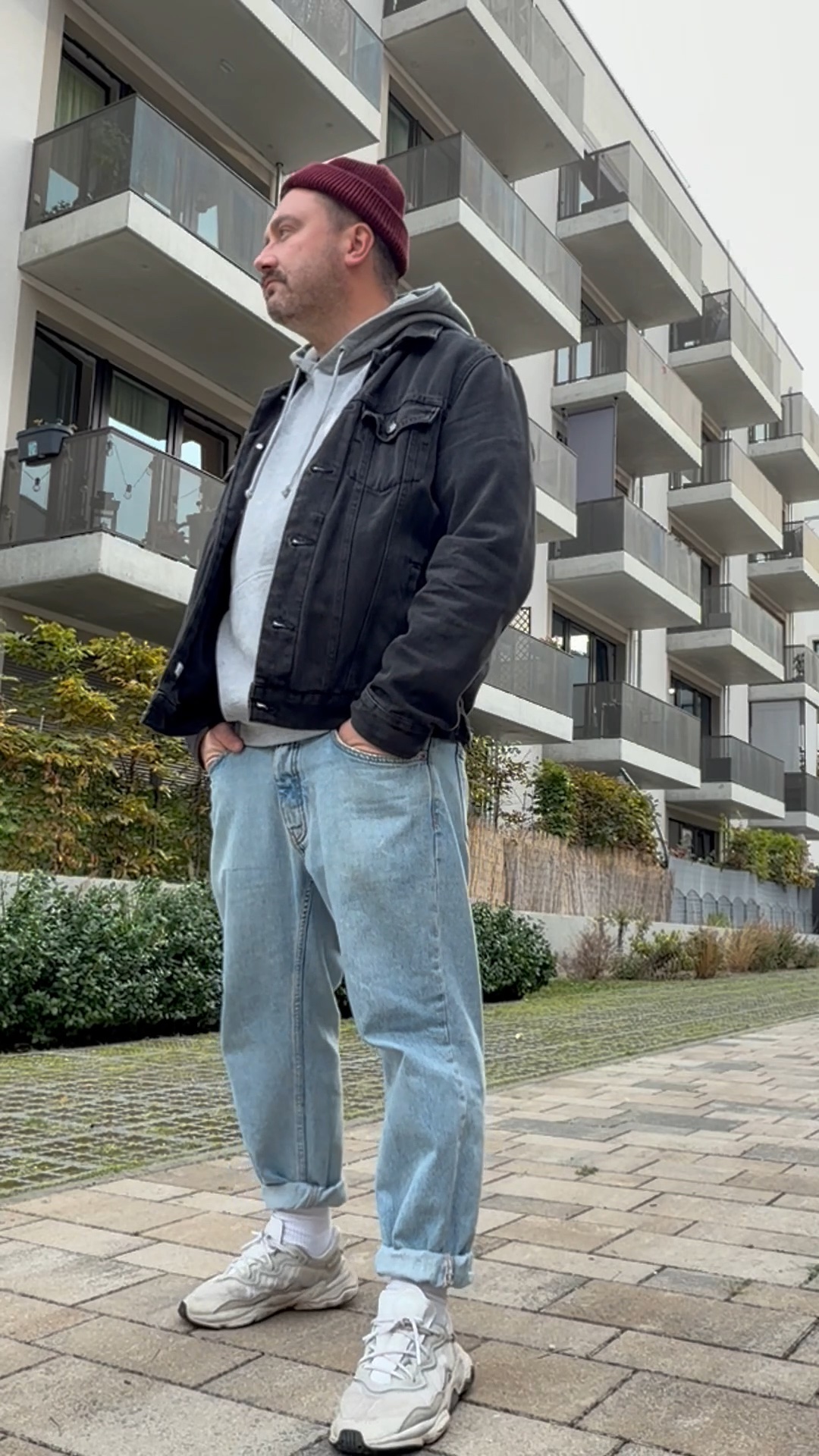 Lässiges Männer-Outfit für den Herbst mit bordeauxroter Strickmütze, schwarzer Jeansjacke, weiter Jeans und hellen Chunky Sneakern